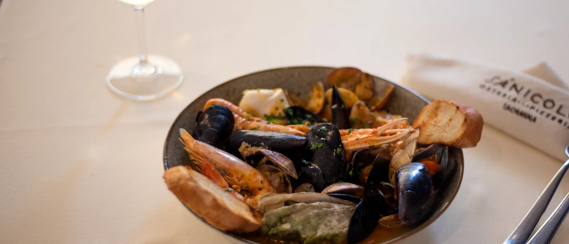 Zuppa di cozze e calice di vino bianco con il logo Sánicolò inciso