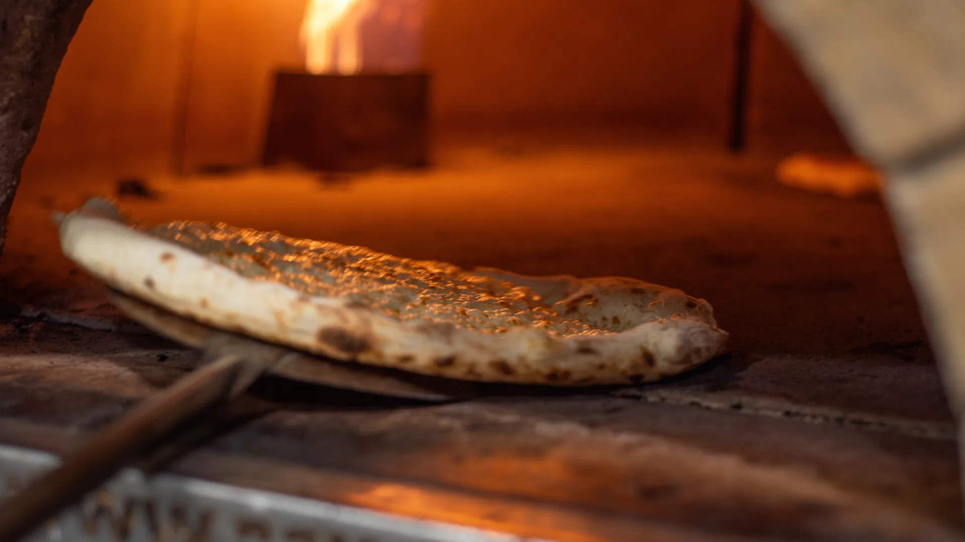 Pizza in cottura nel forno a legna, con la fiamma alta sul lato del forno