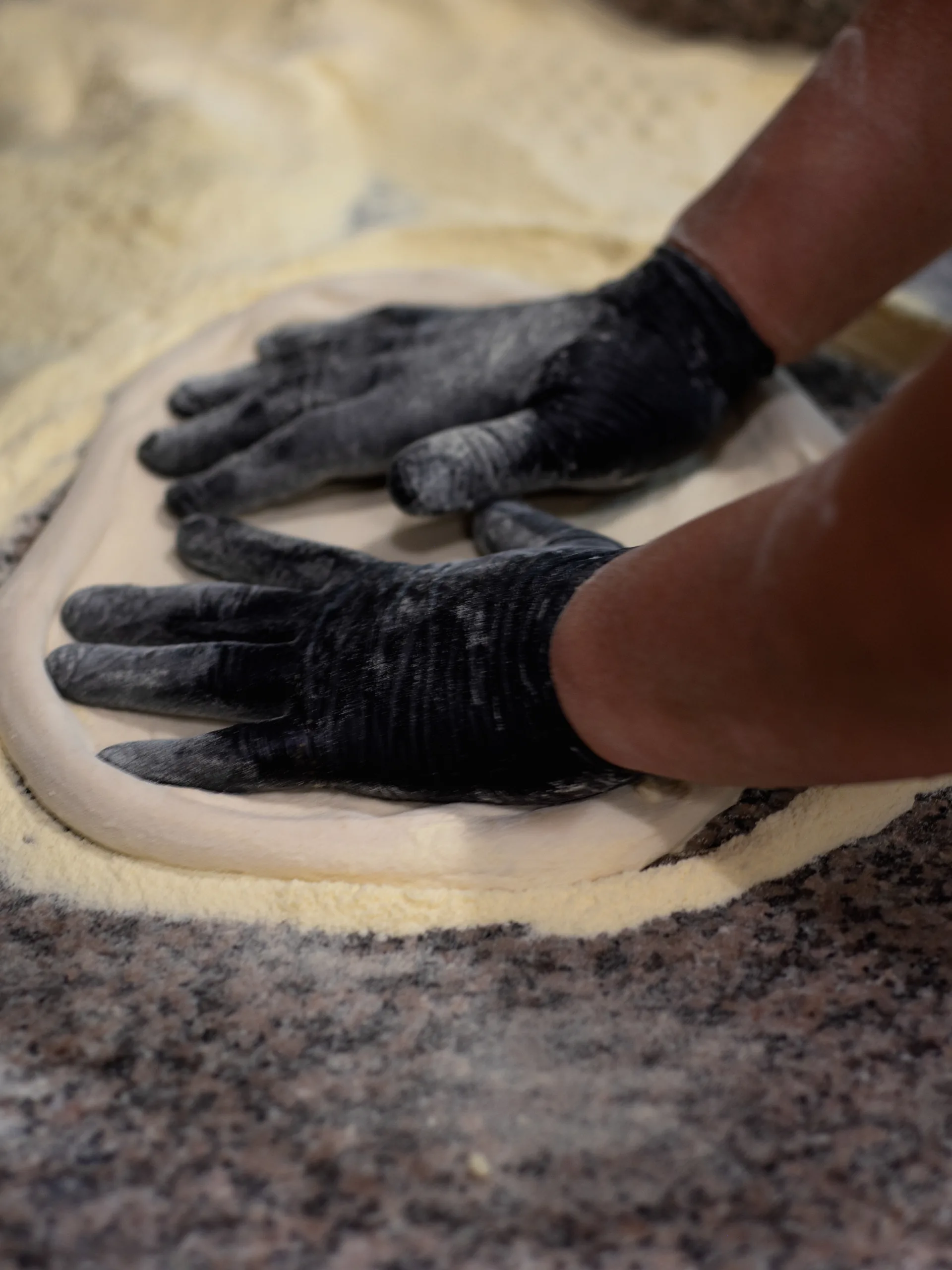 Le mani del pizzaiolo che stendono l'impasto sul marmo infarinato