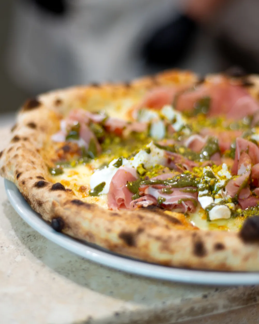 Pizza appena sfornata con crudo, burrata e granella di pistacchio, tenuta in mano dal pizzaiolo