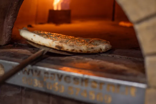La pizza in cottura nel forno a legna, con la fiamma alta di lato